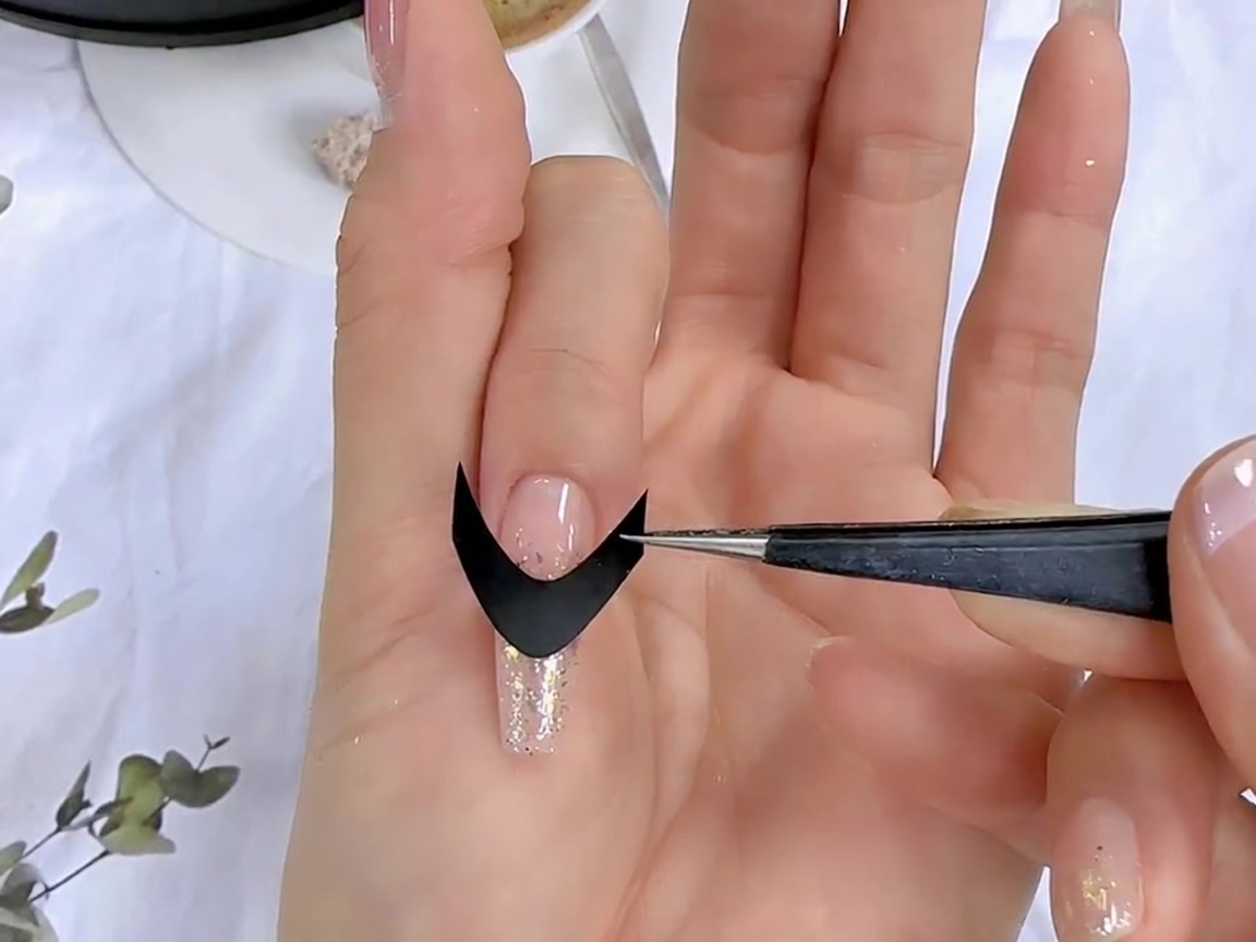 Une paire de pinces positionnant un sticker guide de french manucure noire sur la surface dun ongle préparé.