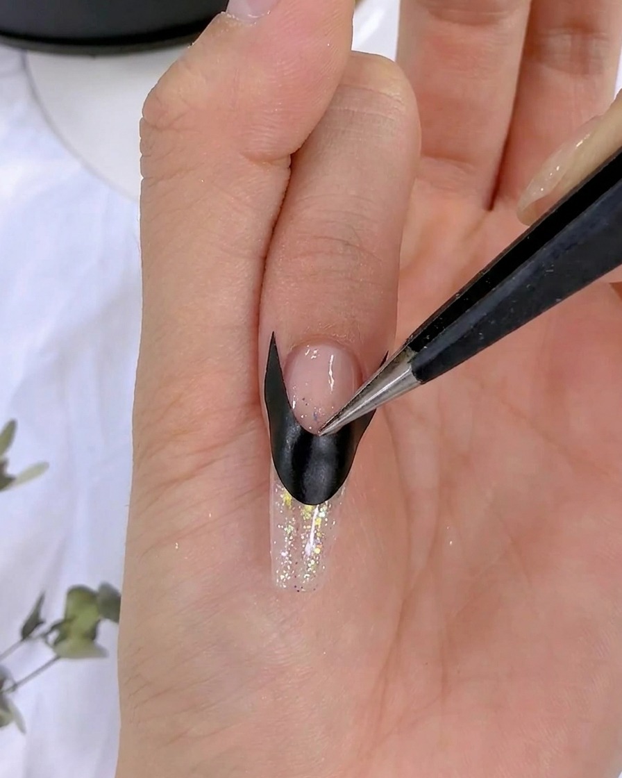 Une pince lissant et fixant un sticker de french noir sur un ongle.
