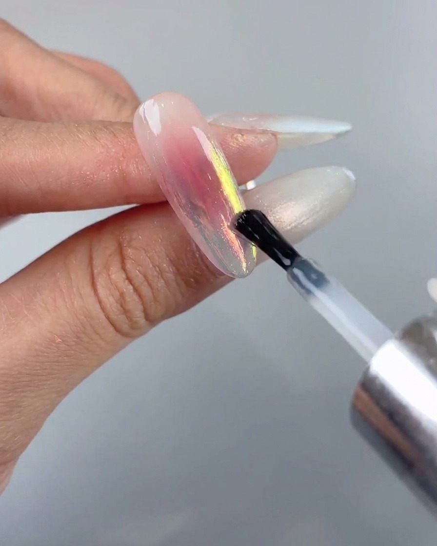 Un pinceau à ongles appliquant une couche de finition lisse sur un design dongle chrome aurora.