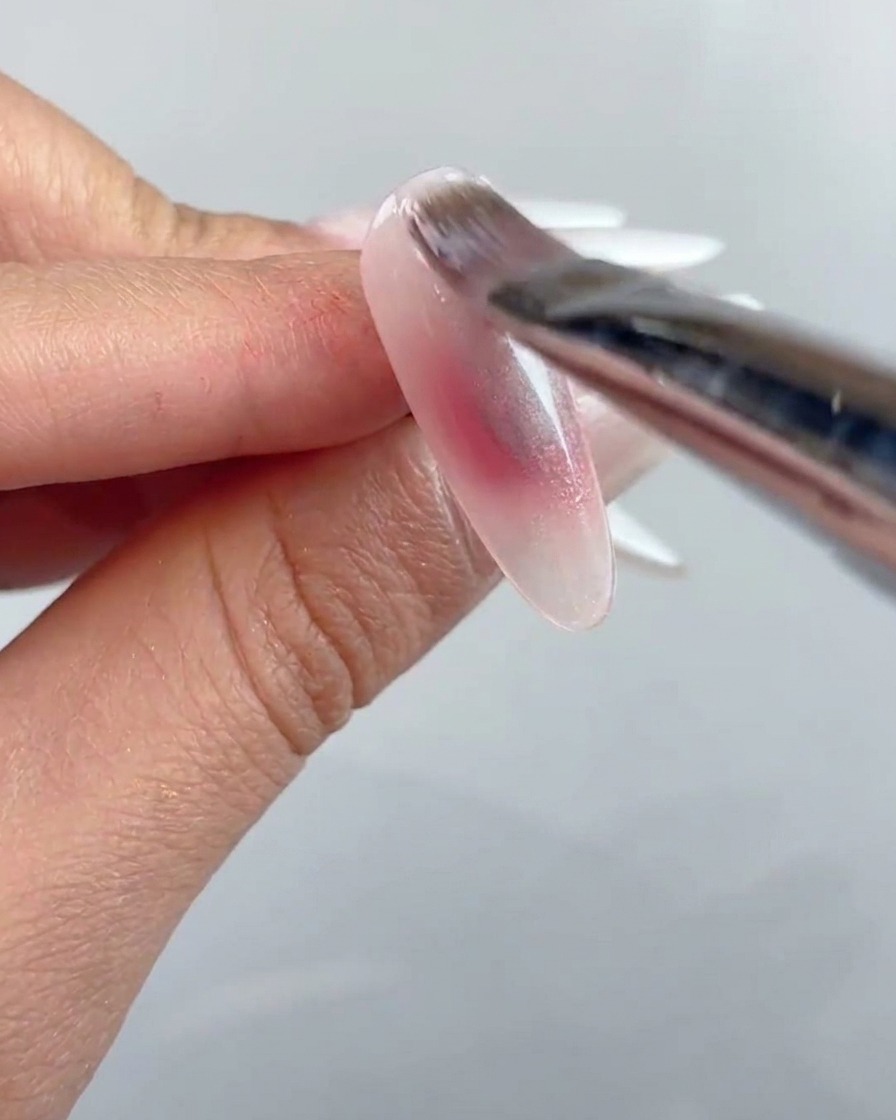 Un pinceau à ongles appliquant une couche de gel cat-eye transparent sur toute la surface de longle préparé.