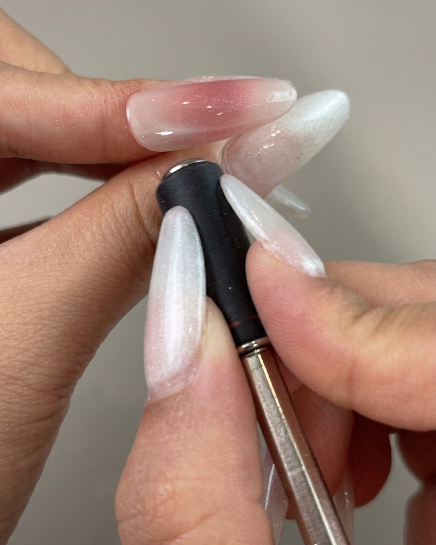 Un bâtonnet aimanté tenu près du côté dun ongle peint pour façonner une ligne de reflet incurvée.