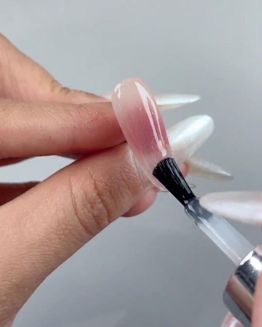 Un pinceau à ongles appliquant une couche de top coat transparent sur un ongle en gel cat-eye catalysé.