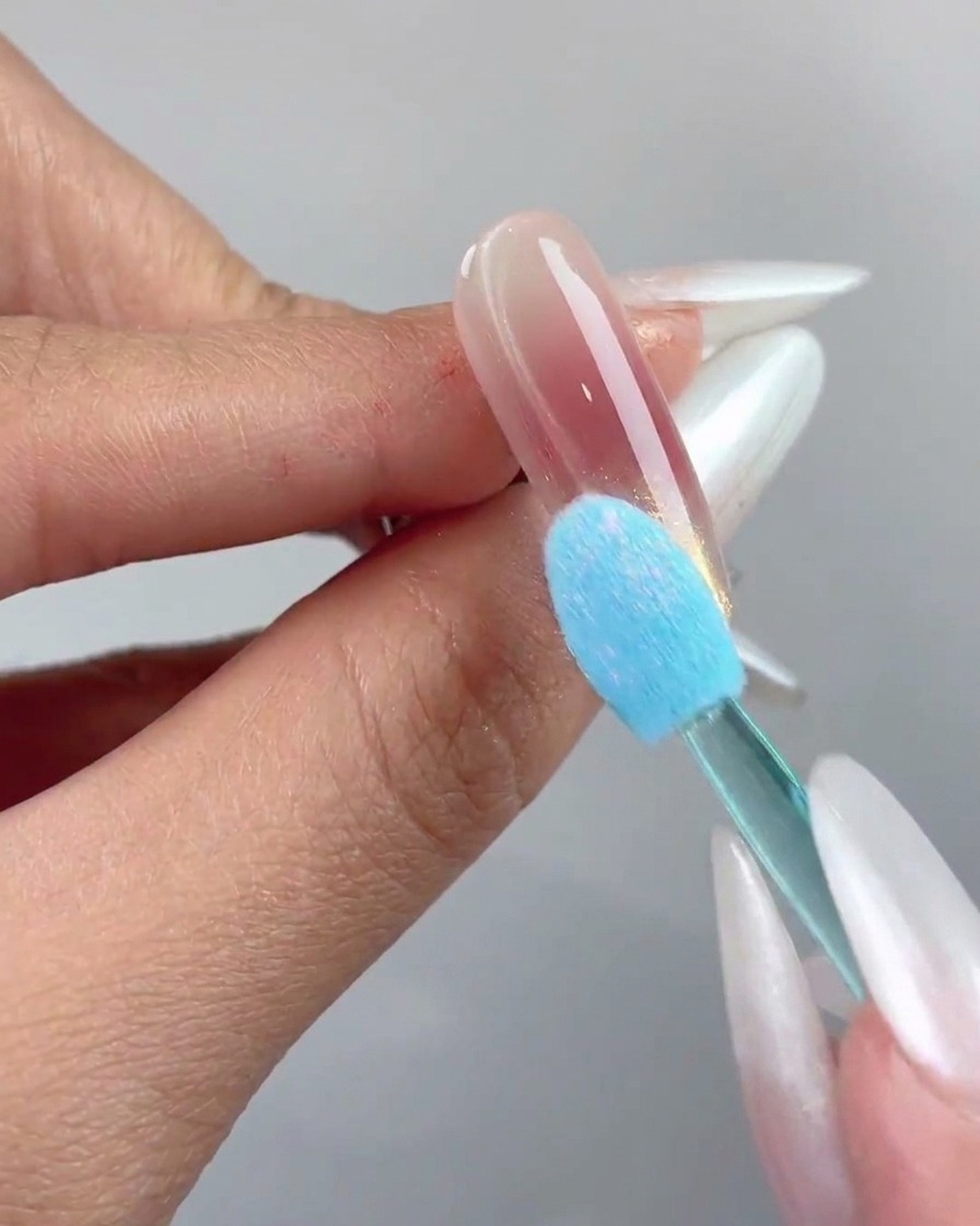 Un applicateur éponge en silicone bleu pressant de la poudre chrome aurora sur le bout dun ongle.