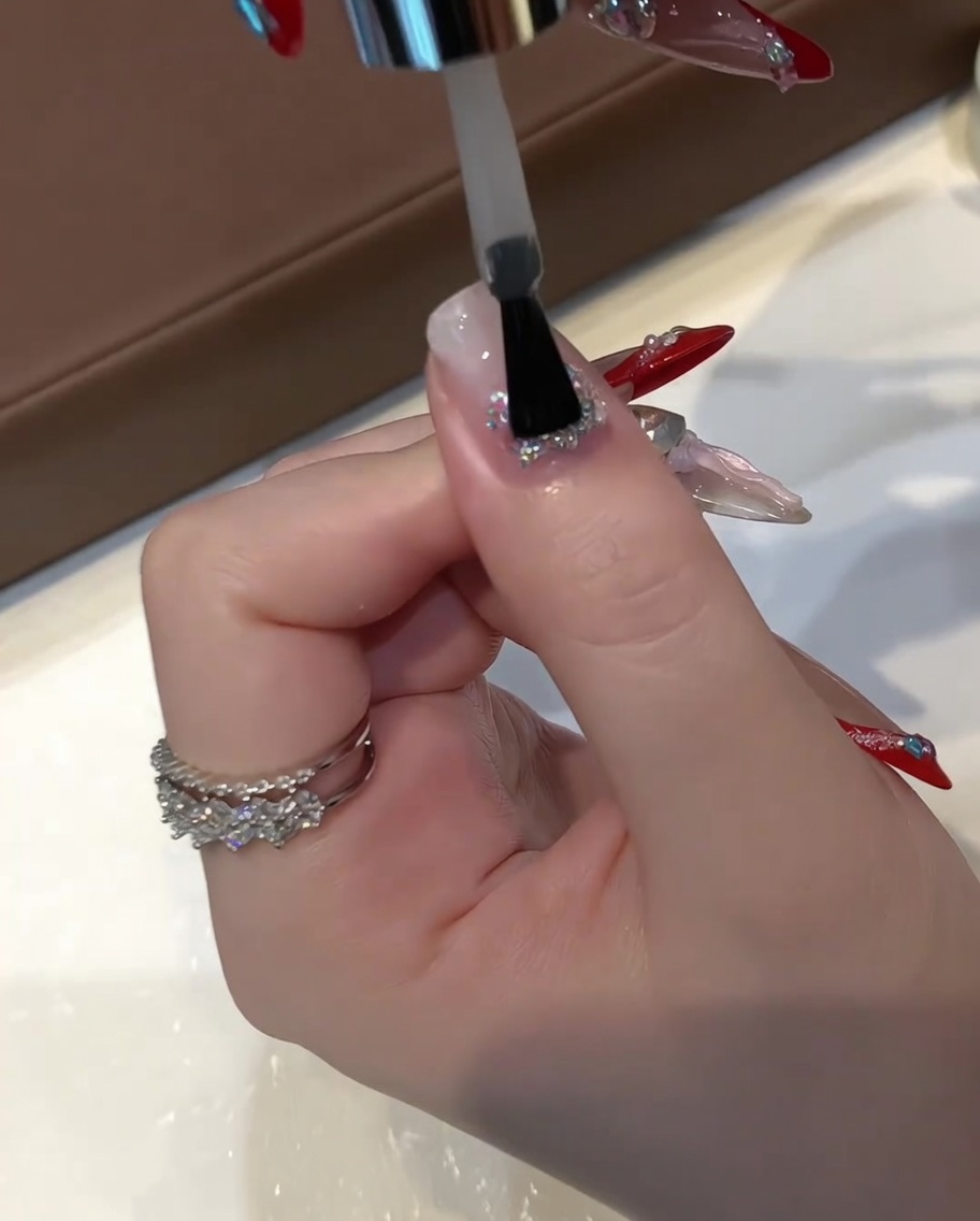 Un pinceau plat à gel appliquant une couche épaisse de gel de construction transparent et auto-égalisant sur un ongle à paillettes encapsulées.