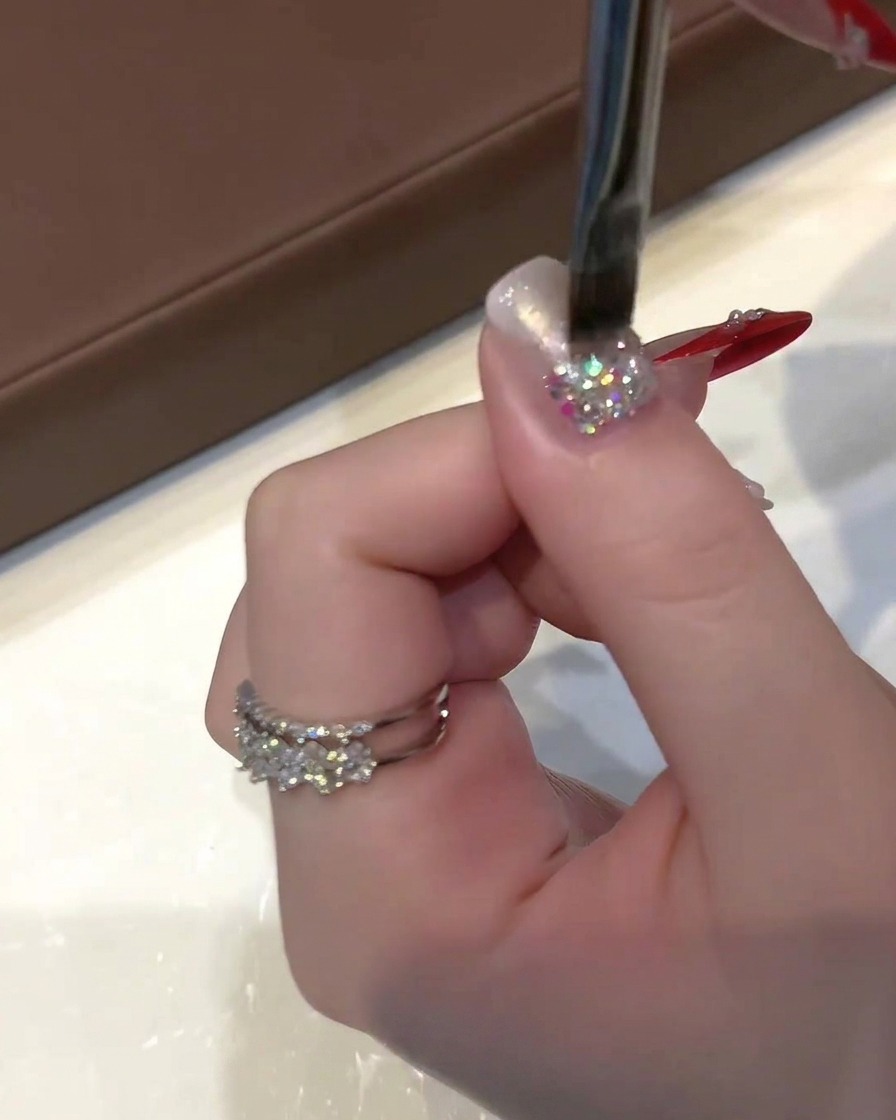 Une main tenant un pinceau plat à gel appliquant un vernis cat-eye doré-argenté translucide sur un ongle pailleté.