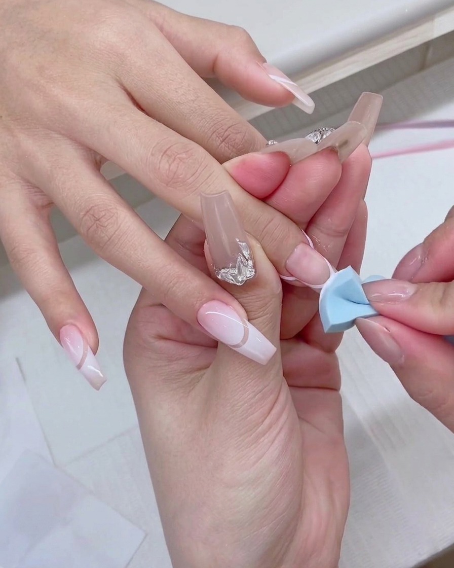 Une éponge à maquillage bleue tapotée doucement sur le bout dun ongle pour créer un effet dégradé blanc.