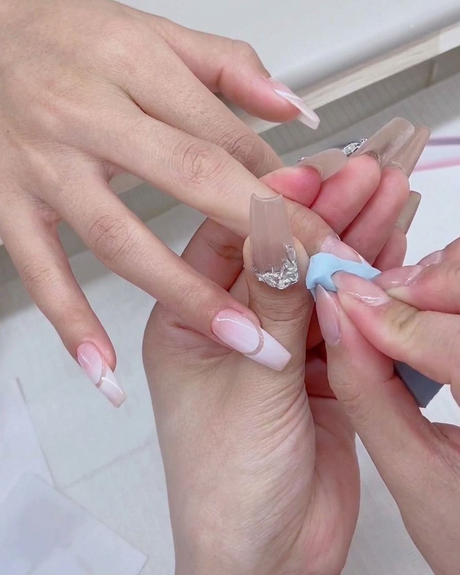 Un pinceau de vernis en gel appliquant du produit blanc frais directement sur le bord dune éponge à maquillage bleue.