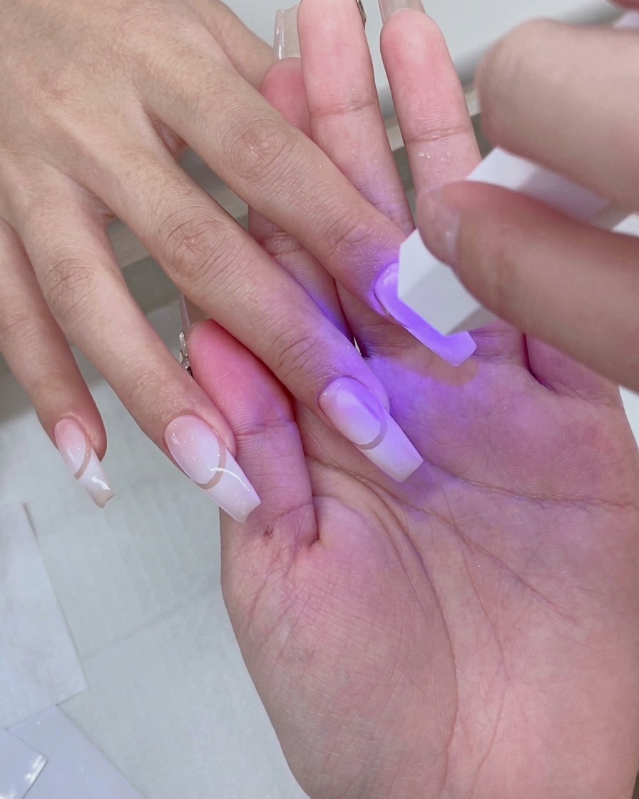 Une main reposant à lintérieur dune lampe à ongles UV/LED rose avec une lumière violette illuminant les ongles dégradés préparés.