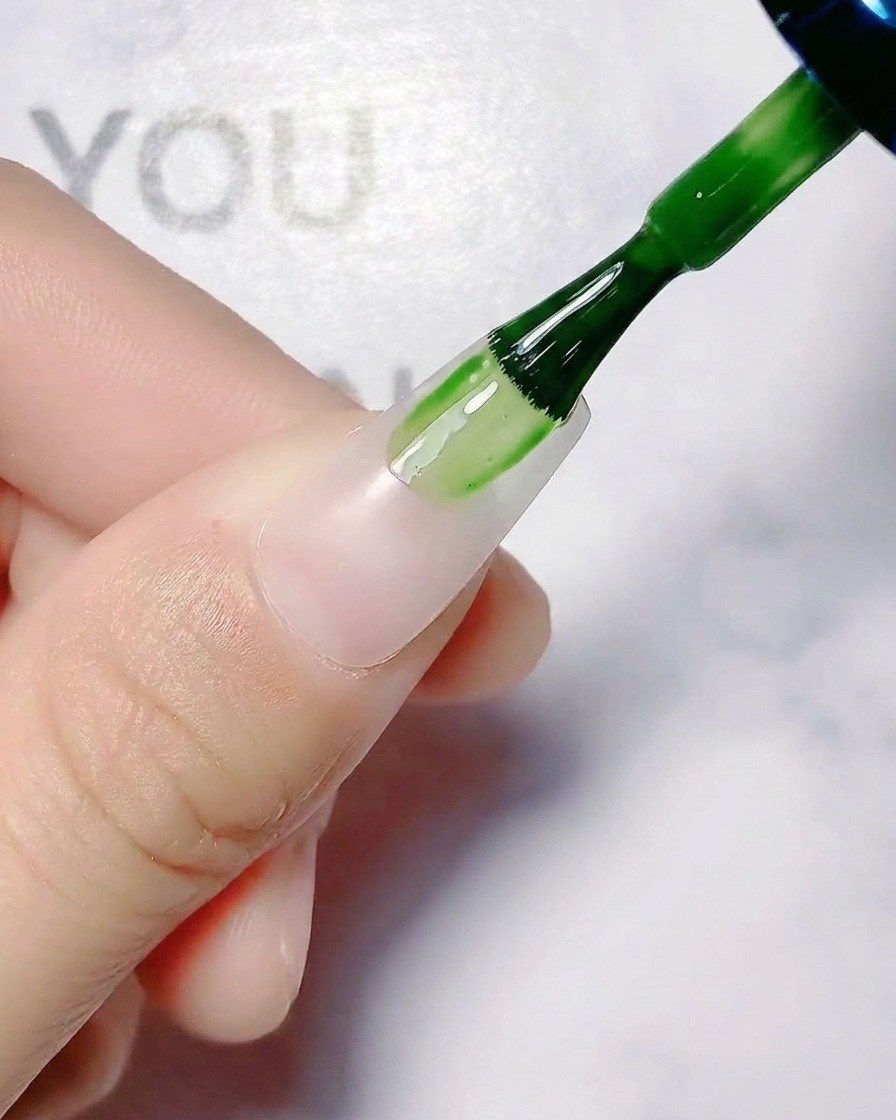 Un pinceau appliquant une couche de base blanche translucide sur un ongle naturel.