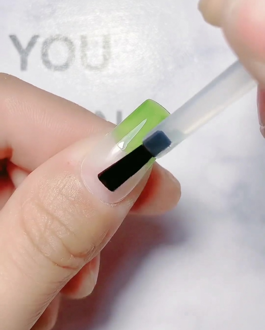 Un pinceau appliquant du gel vert olive sur la partie supérieure dun ongle naturel.