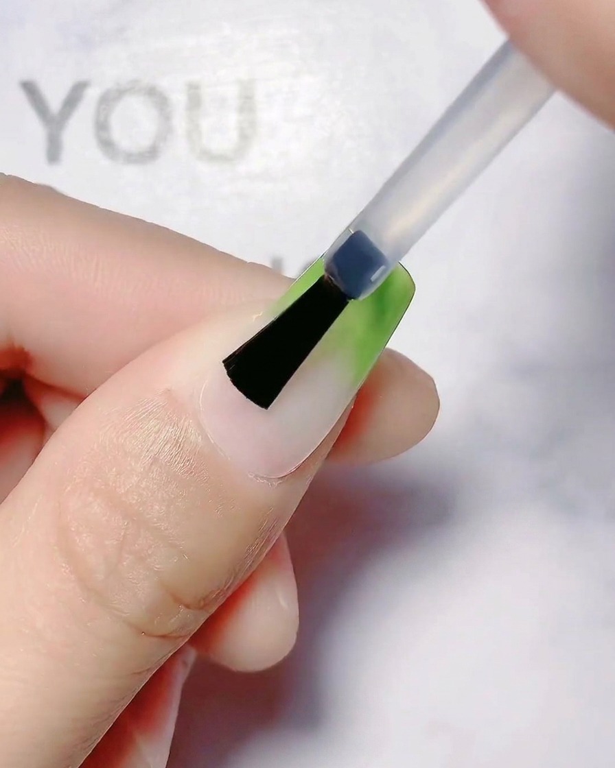 Un pinceau lissant la transition du dégradé vert olive sur un ongle.