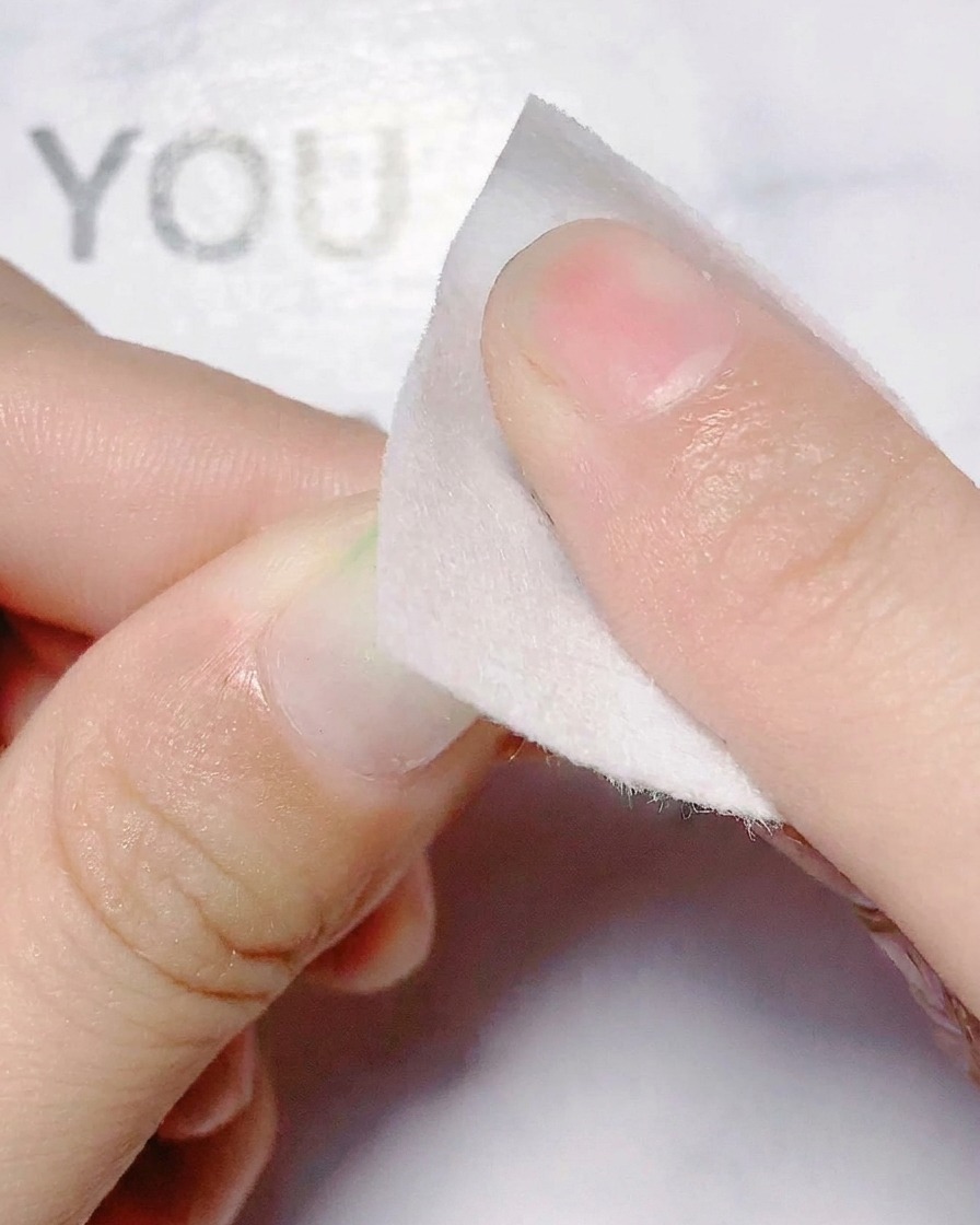 Un doigt appliquant un sticker découpé en forme de fleur holographique sur un ongle.
