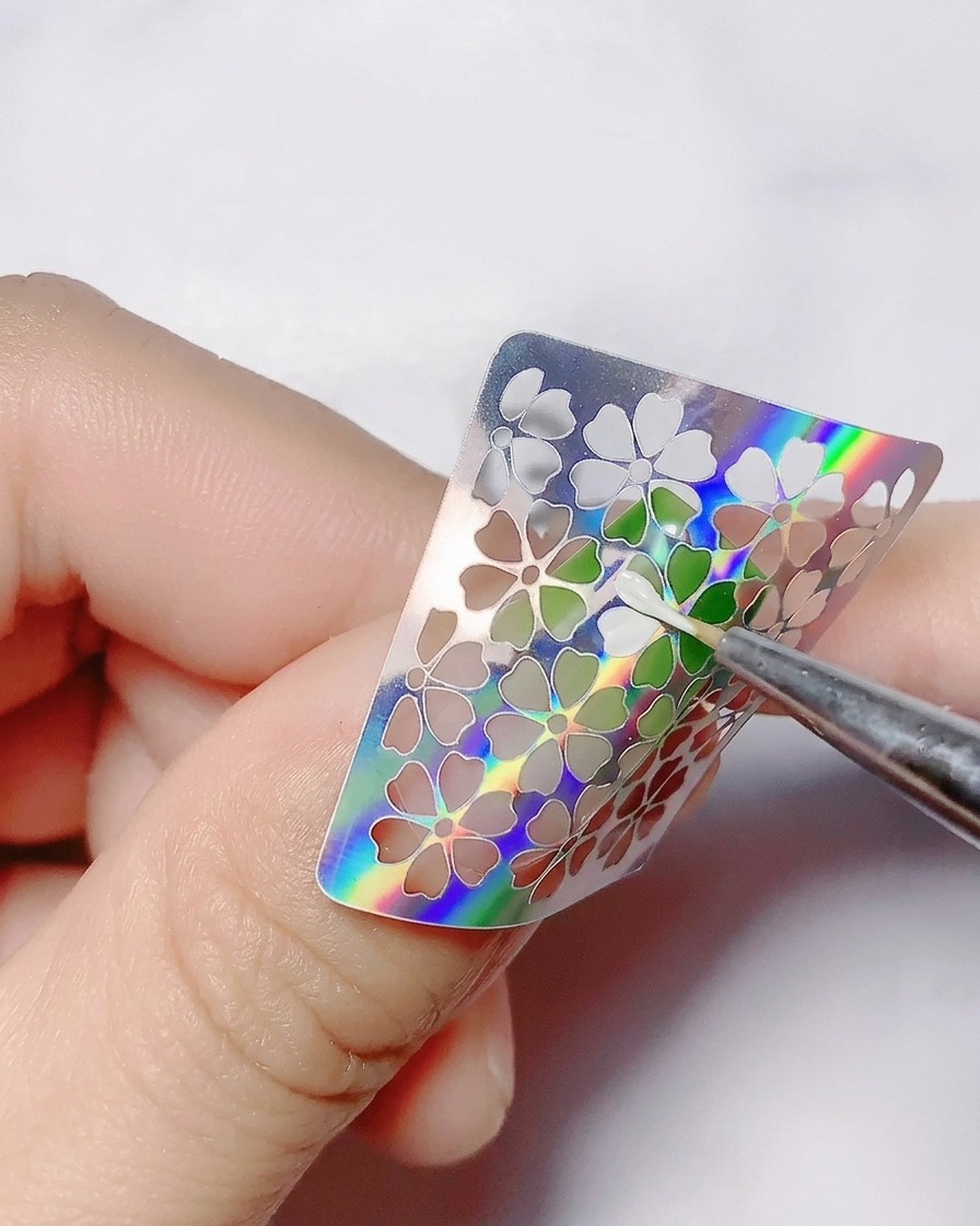 Un pinceau fin appliquant du gel blanc à lintérieur des découpes dun sticker fleur.