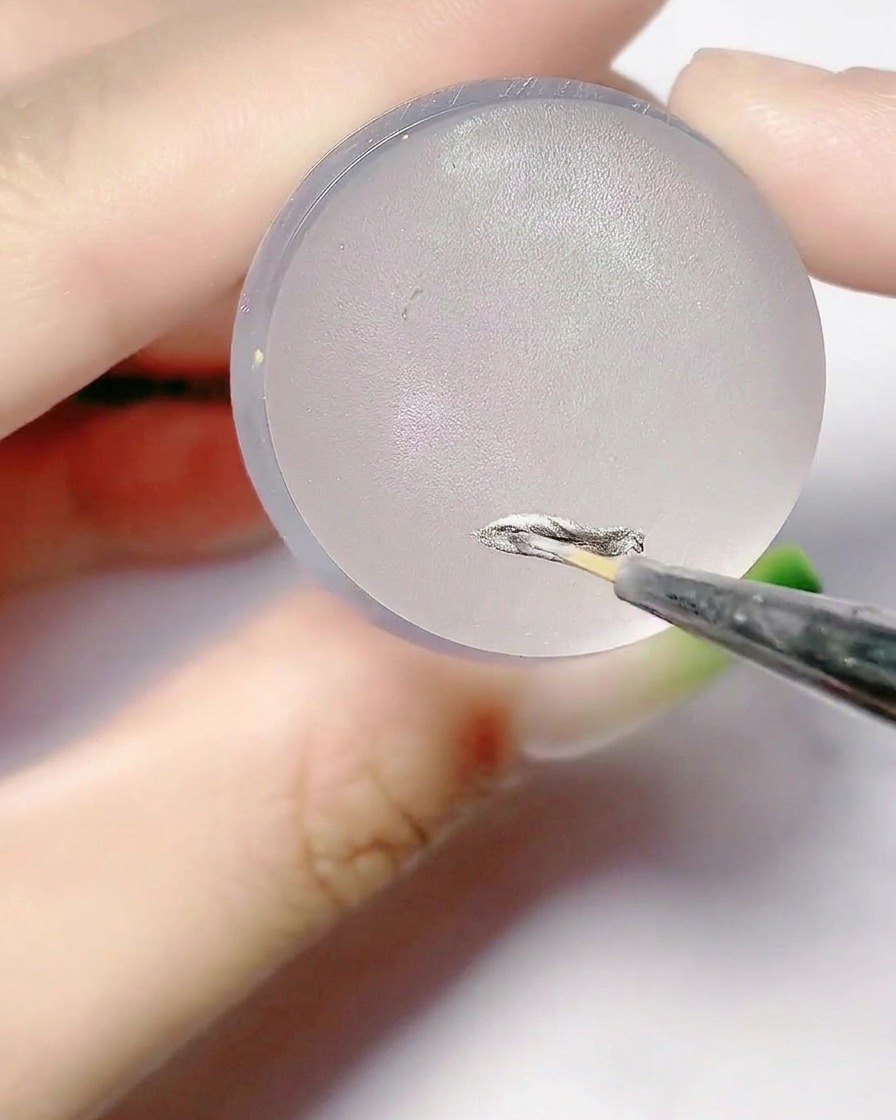 Un pinceau fin appliquant du gel argenté sur la surface plate dun tampon en silicone.