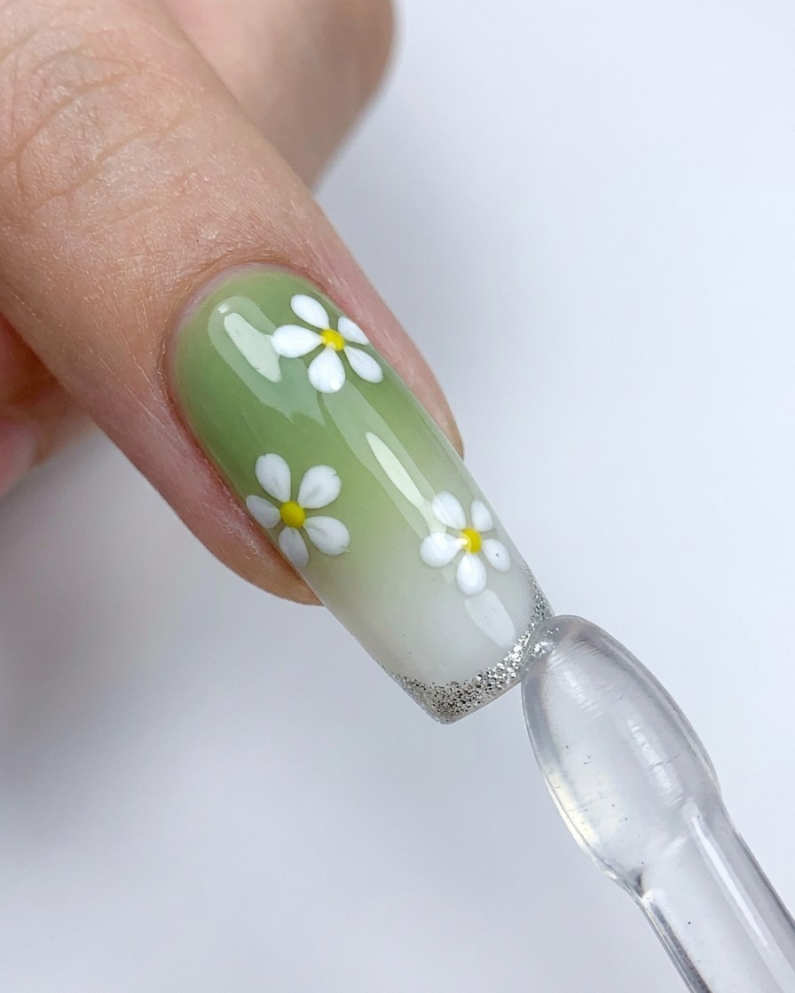 Un ongle décoré de fleurs blanches pressé contre un tampon en silicone pour appliquer une french argentée.