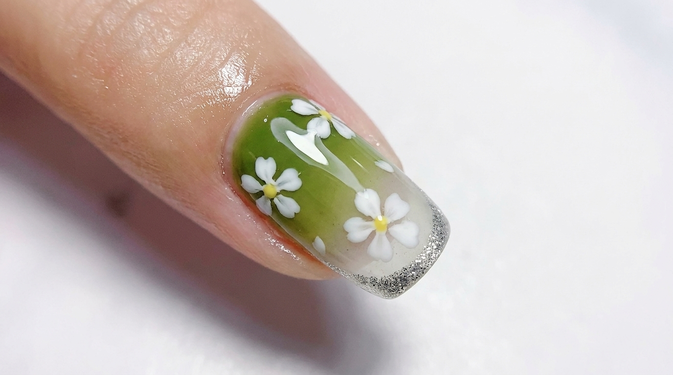 Ongle en gel dégradé du vert olive brillant au blanc translucide, orné de fleurs blanches à cinq pétales et dune fine french manucure argentée pailletée.