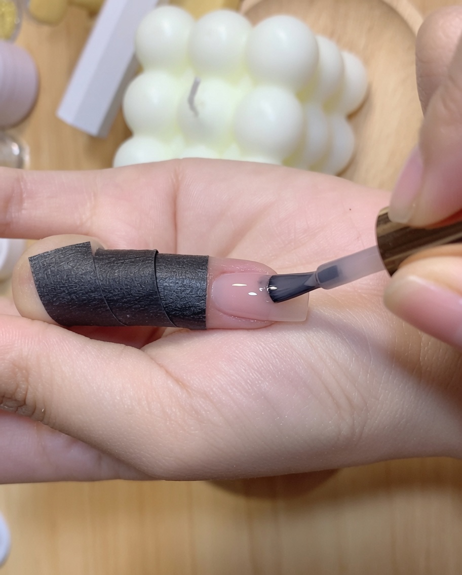 Une main tenant une lampe à polymériser au-dessus dun ongle recevant sa deuxième couche de couleur.
