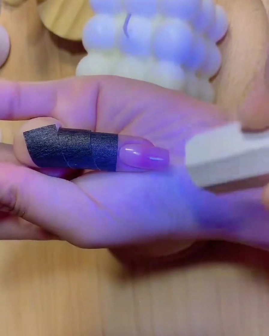 Une main positionnée dans une lampe à ongles UV/LED avec une lumière bleue illuminant les doigts et longle dégradé catalysé.