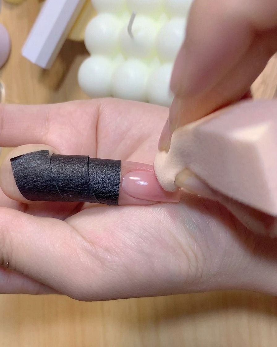Une éponge à maquillage tapotant de la couleur rose sur un ongle pour intensifier le dégradé ombré.