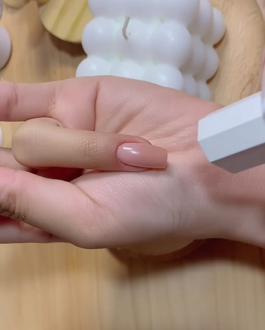 Une main manucurée avec un ongle au dégradé rose intensifié positionnée près dune lampe UV blanche.