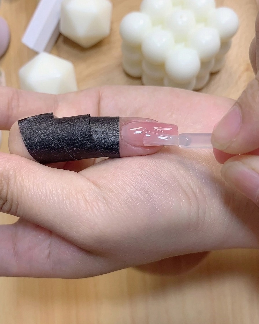 Un petit pinceau appliquant une couche transparente de gel de renforcement sur un ongle coloré en dégradé.