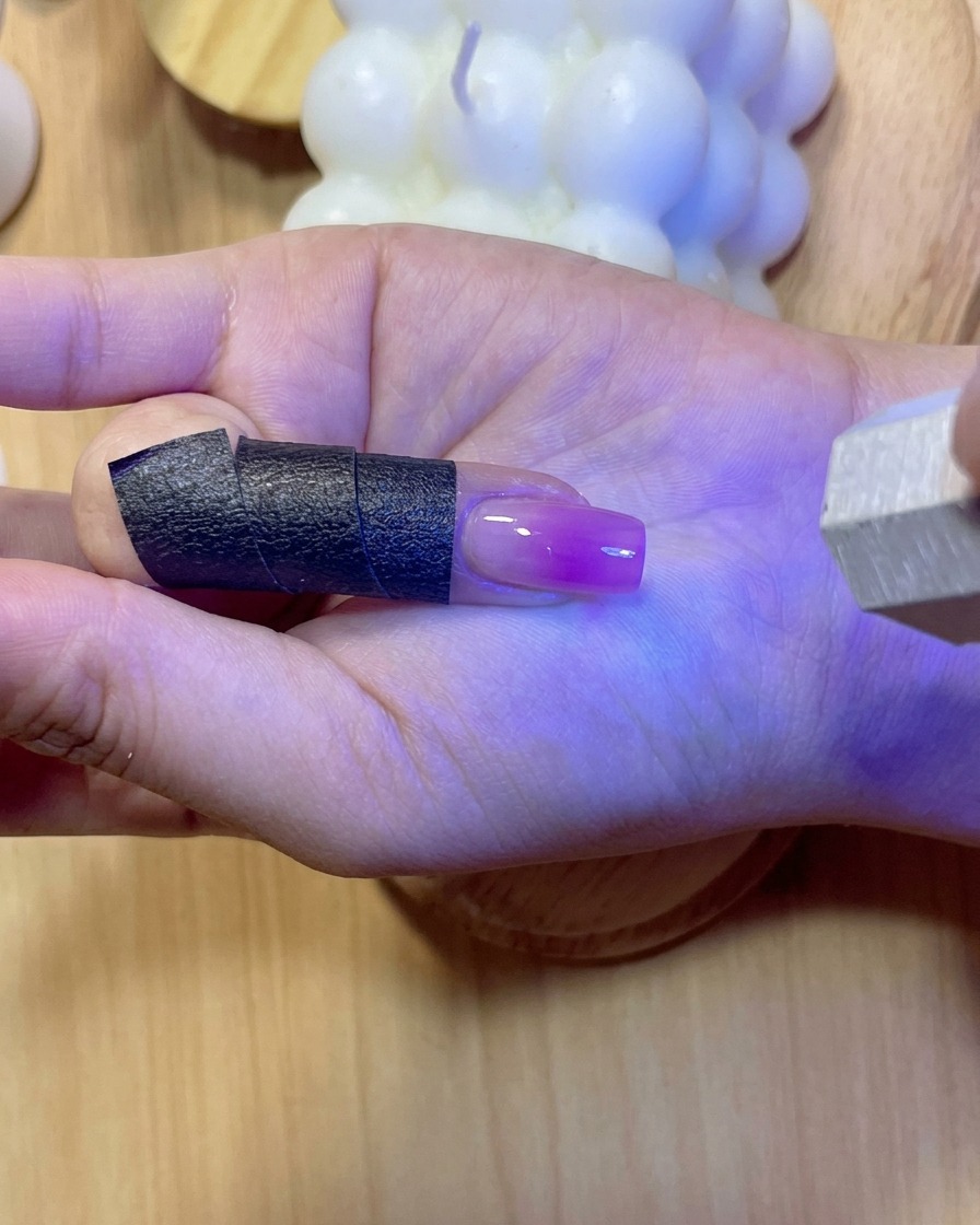 Un ongle brillant sous une lumière UV/LED violette pendant la polymérisation du gel de renforcement.