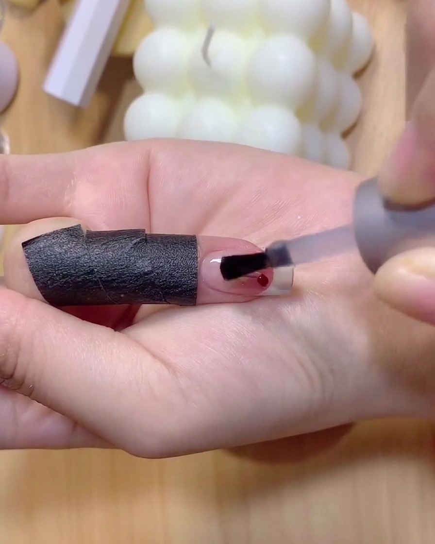 Un pinceau fin pour ongles appliquant du vernis gel marron clair pour dessiner de fines tiges de cerise.
