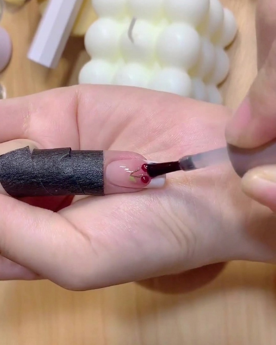 Un ongle avec des tiges de cerises peintes placé sous une lampe à polymériser.