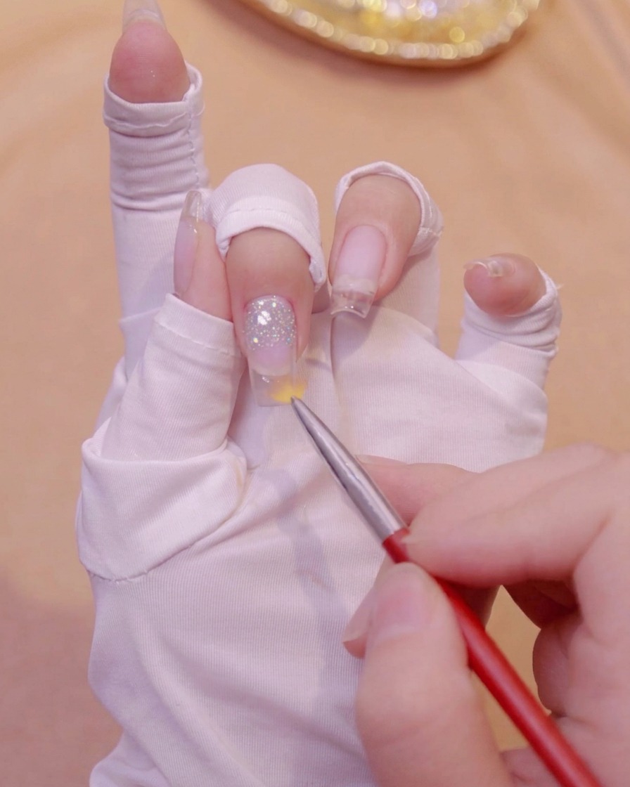 Un pinceau à dégradé balayant vers le bas sur un ongle transparent pour estomper le gel pailleté.