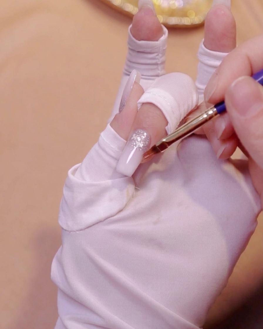 Un pinceau à dégradé lissant la deuxième couche de gel blanc laiteux sur un ongle.