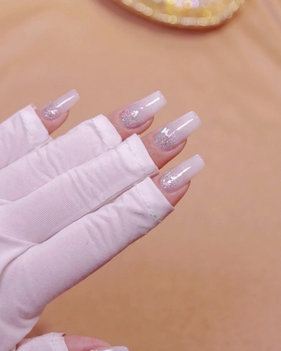 Une main placée à lintérieur dune lampe à ongles UV LED catalysant la couche de dégradé blanc laiteux.