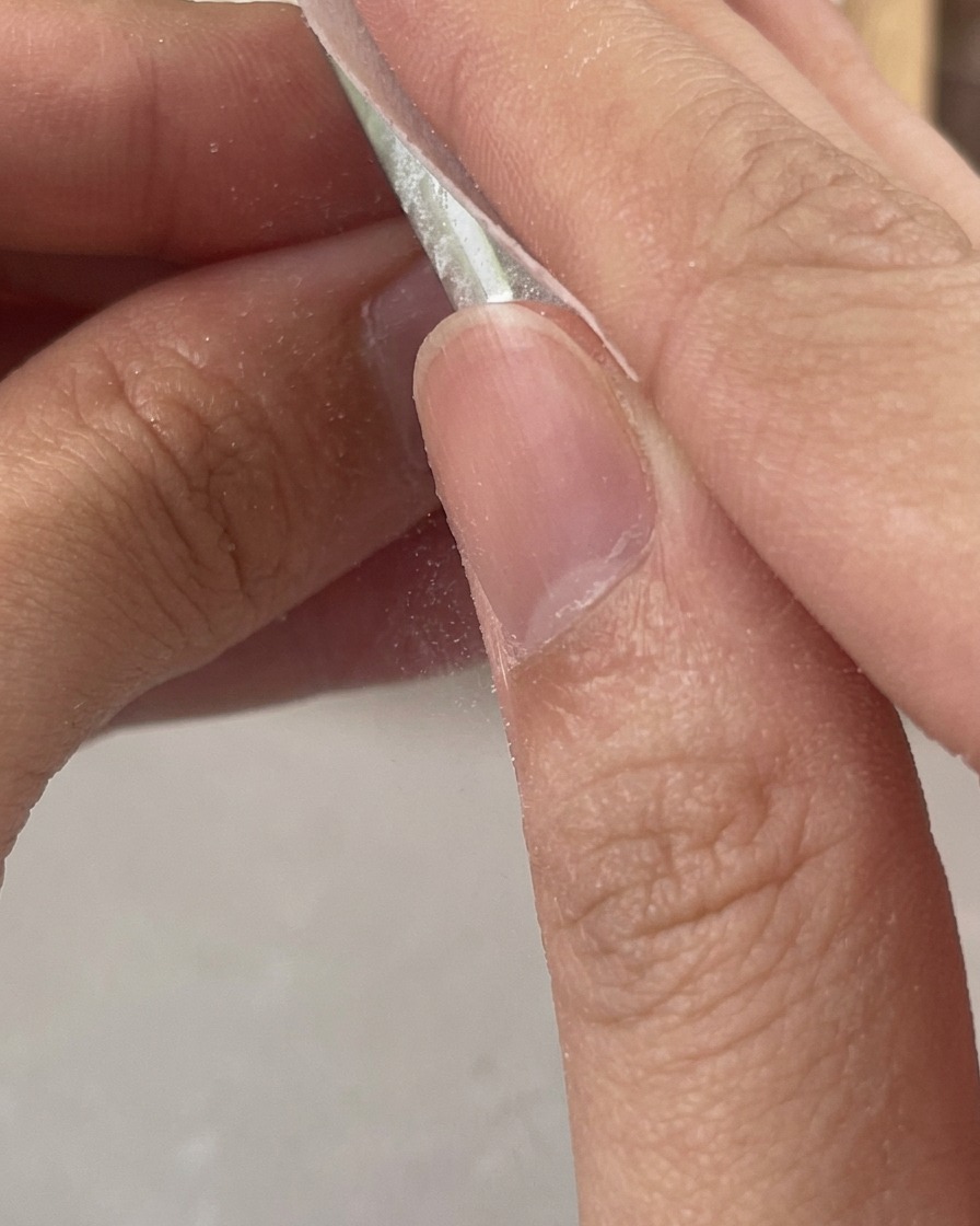 Des doigts utilisant un coton non pelucheux pour nettoyer le résidu collant dun ongle en gel transparent fraîchement catalysé.