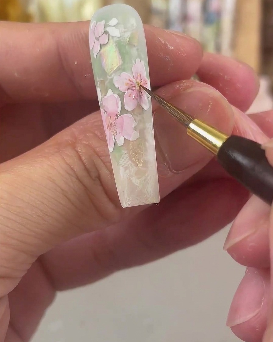 Un pinceau de détail fin déposant de laquarelle jaune vif au centre des pétales floraux teintés de rose.