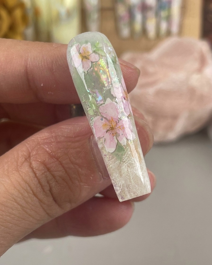 Un ongle brillant et encapsulé montrant des fleurs aquarelles roses et jaunes scellées sous une épaisse couche de gel transparent.