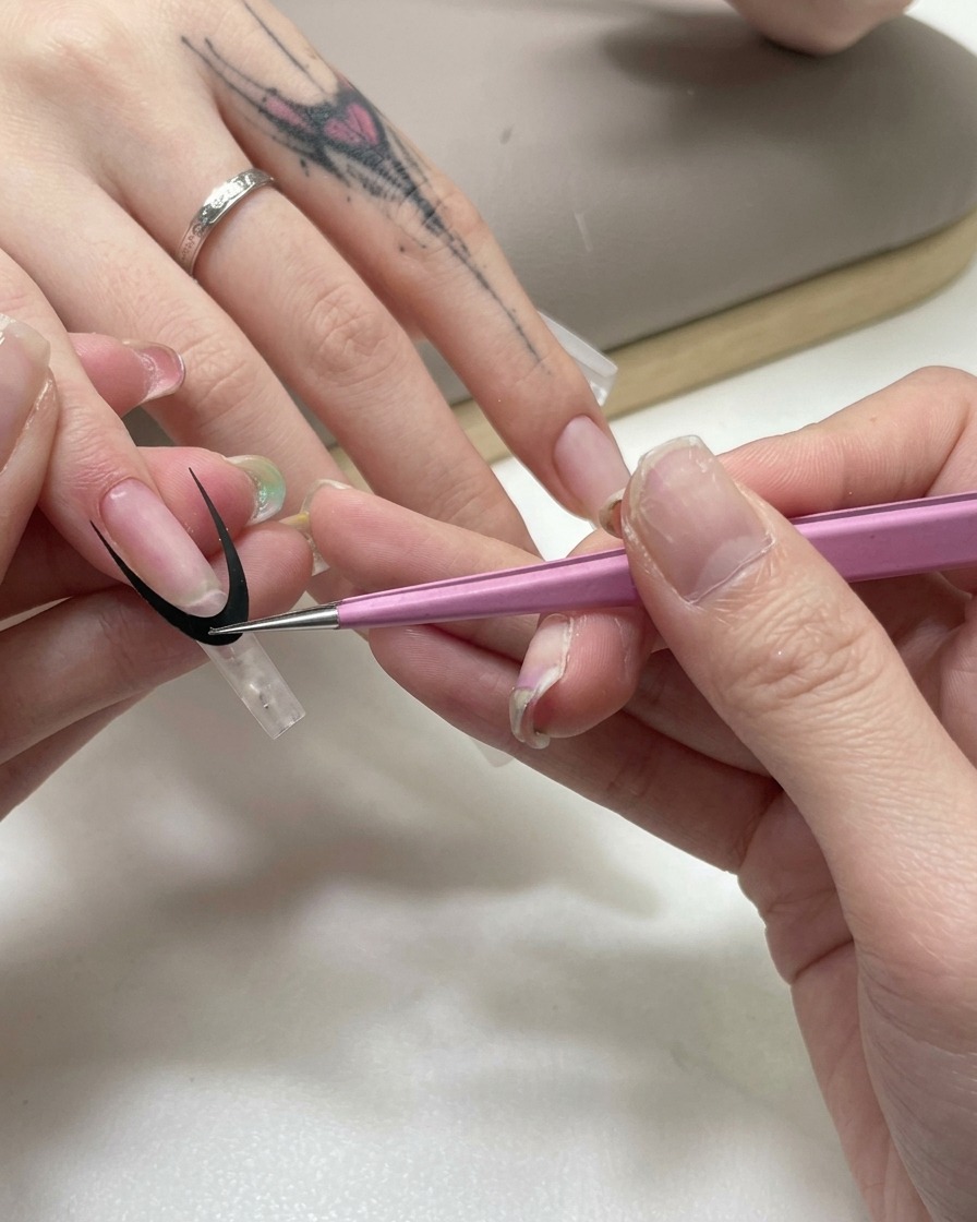 Une pince à épiler rose appliquant un autocollant noir incurvé pour french manucure sur une capsule transparente.