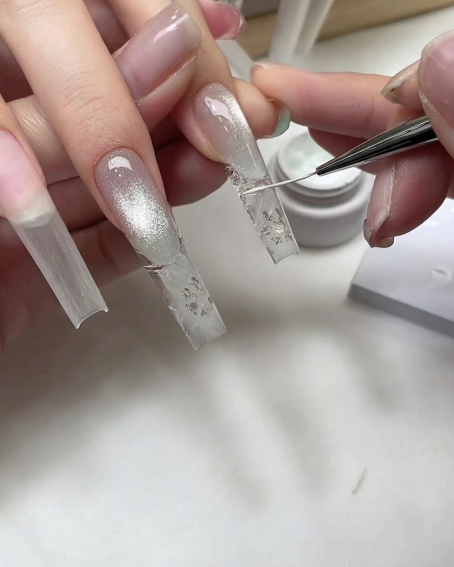 Un pinceau fin pour nail art dessinant des détails de flocon de neige blanc sur une capsule transparente texturée.