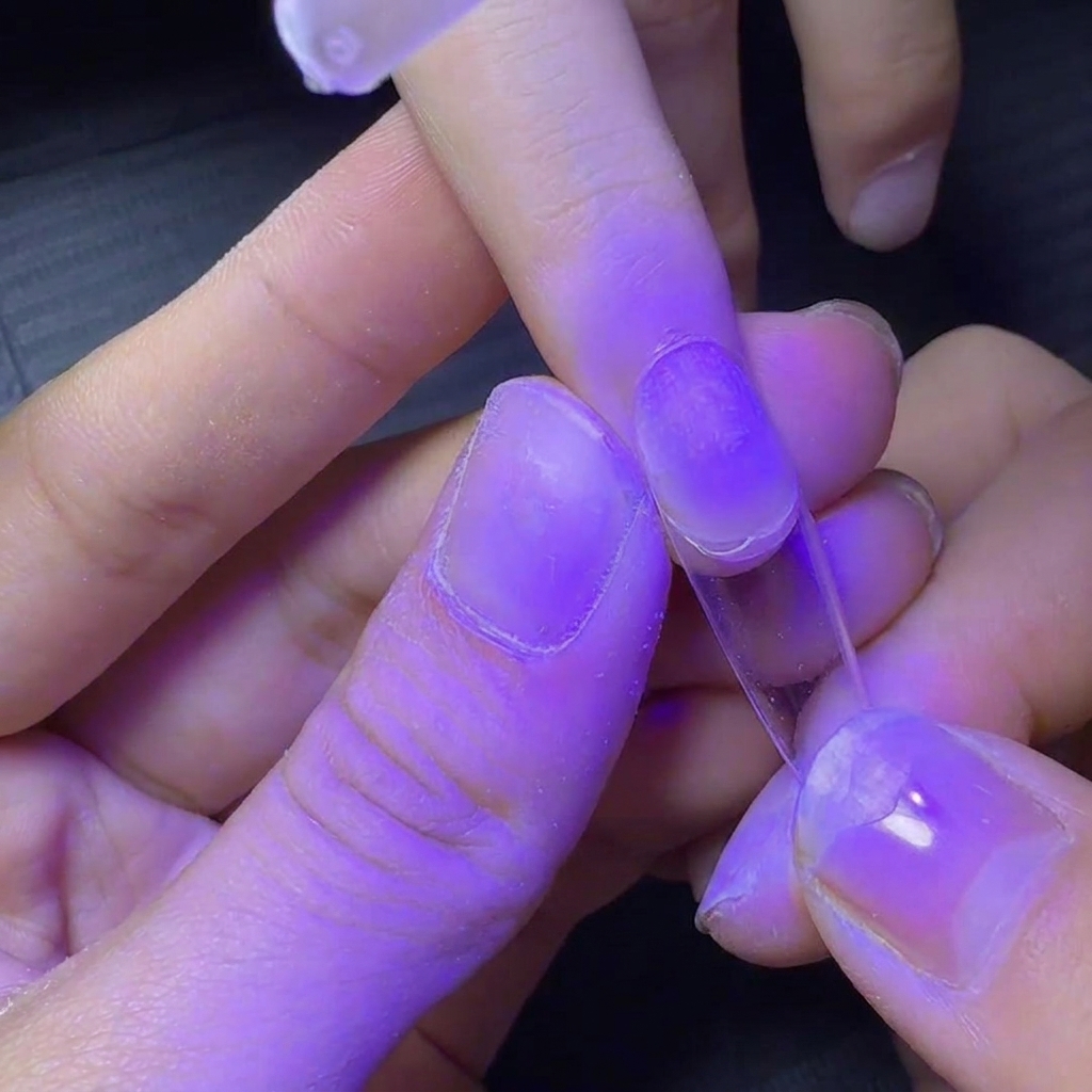 Un ongle avec une capsule transparente maintenu sous une lampe UV violette pour une catalysation rapide.