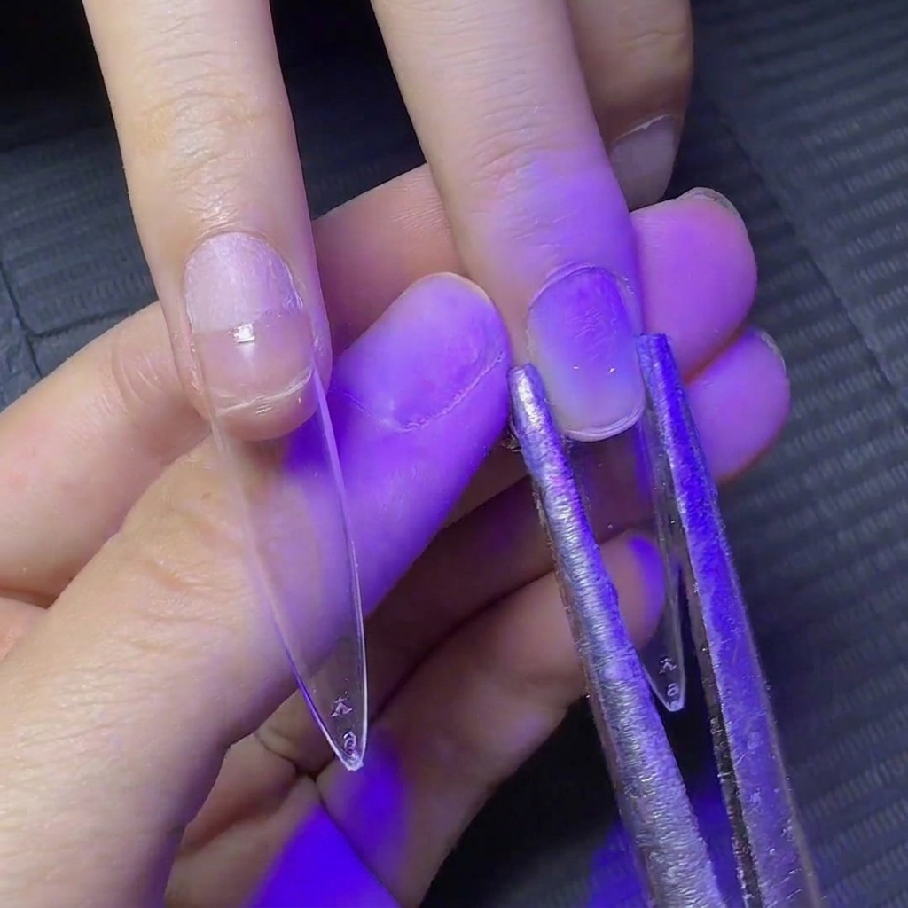 Une pince en métal serrant les côtés dune extension dongle transparente sous lumière UV pour façonner la courbure.
