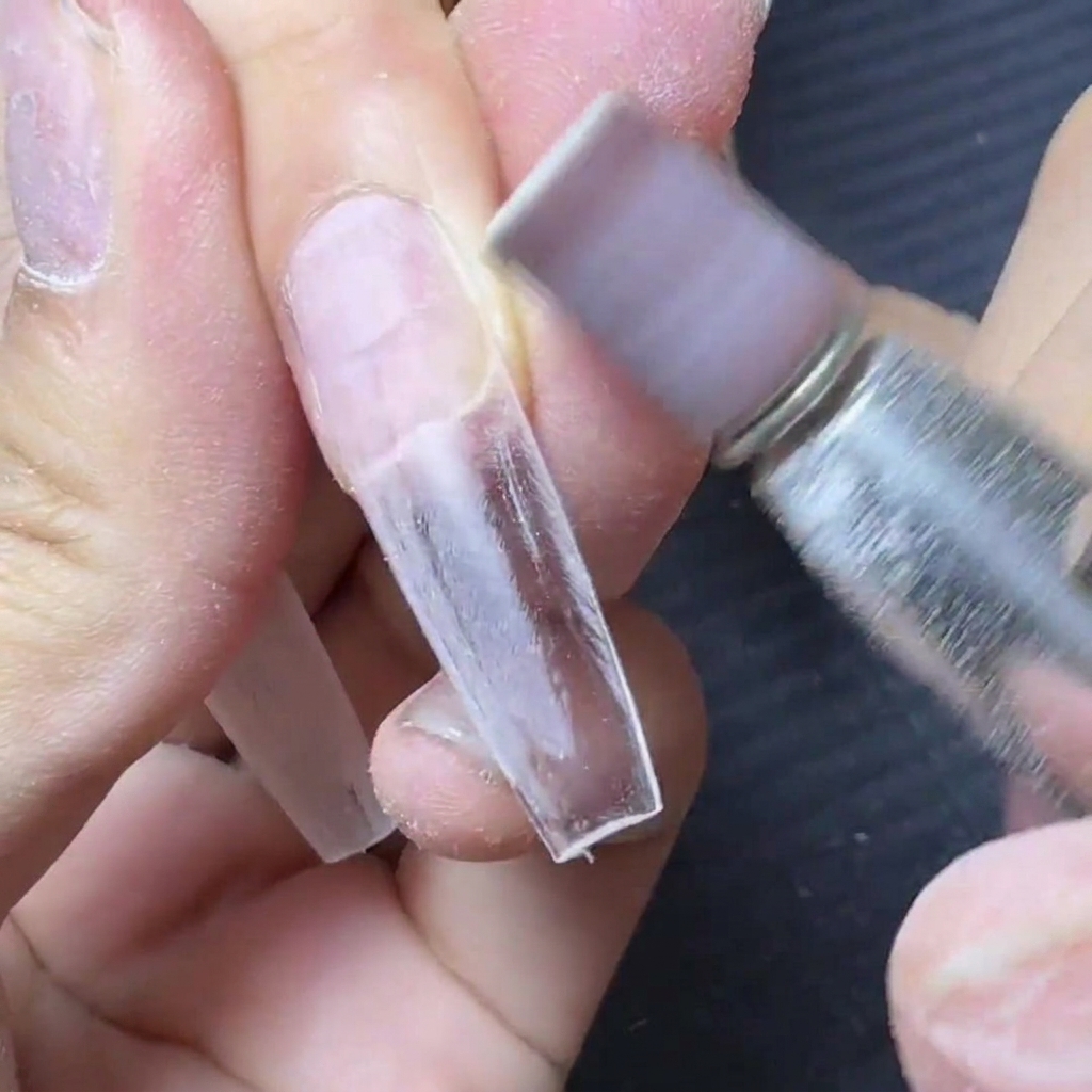 Une ponceuse électrique avec un embout émeri lissant la zone de jonction dune extension dongle transparente.