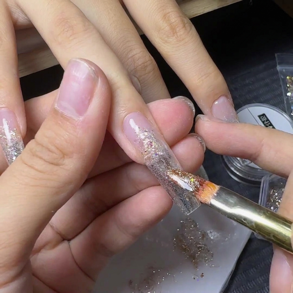 Un pinceau appliquant des flocons de paillettes jaune-or scintillants sur le centre dun ongle décoré.