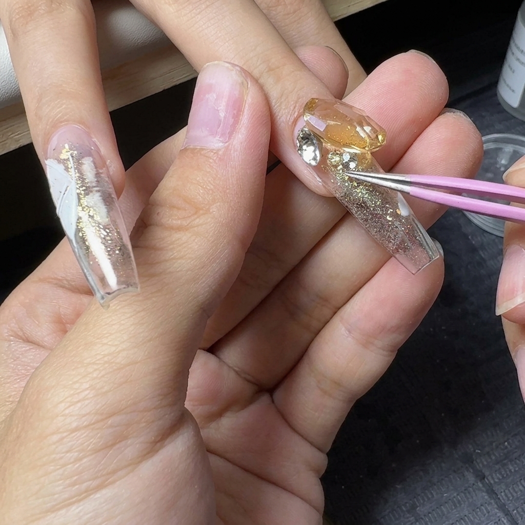 Des pincettes de précision plaçant de petits strass en cristal autour dune grande pierre précieuse centrale sur un ongle à paillettes.