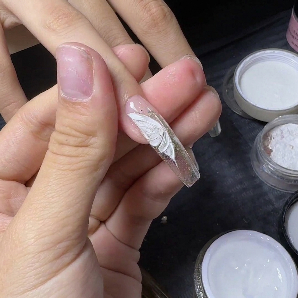 Le pouce dun manucure tenant un ongle pour fixer un petit strass argenté sur un papillon blanc peint.