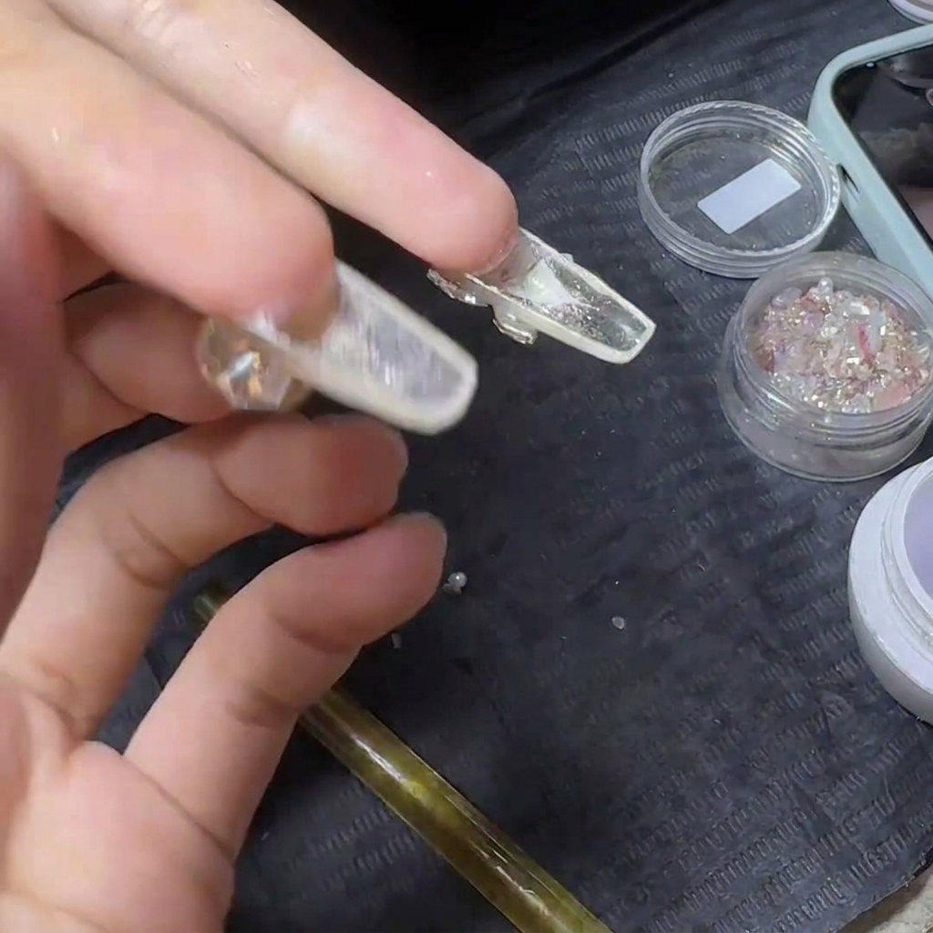 Une main tenant une extension dongle transparente finie retournée à lenvers, exposant le dessous transparent pour lapplication dun top coat.