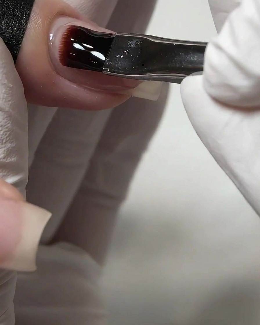 Un pinceau à ongle appliquant une couche épaisse de gel de construction transparent auto-égalisant sur un ongle.