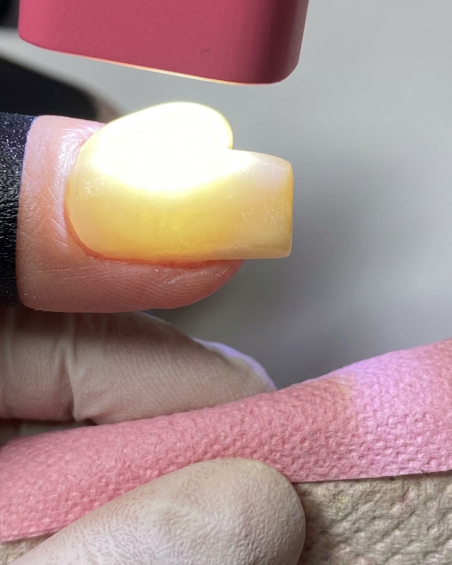 Une lampe UV rose portable en train de catalyser le vernis gel jaune sur un ongle.