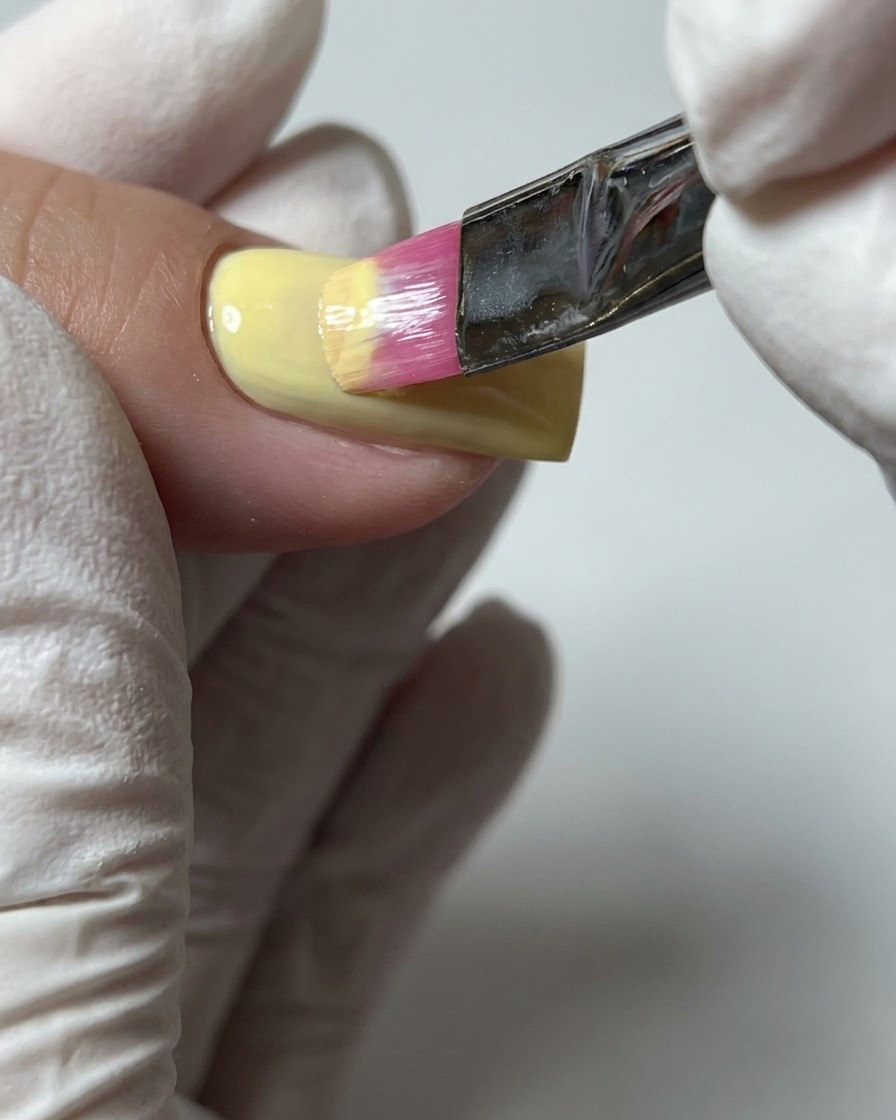 Gros plan dun pinceau appliquant une seconde couche de vernis gel jaune pastel pour assurer une couverture de couleur complète.