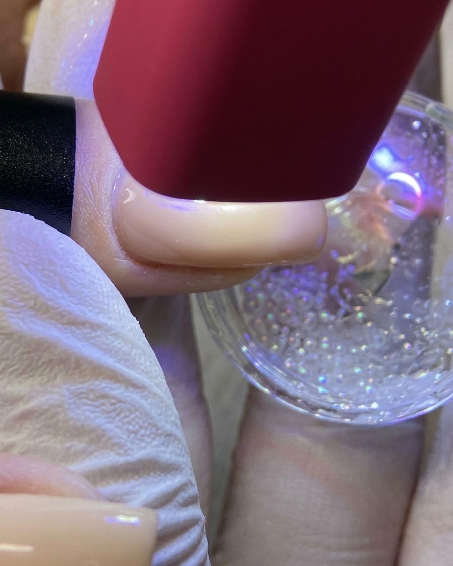 Une lampe UV/LED rouge portable éclairant un ongle pour catalyser un motif détoile blanche recouvert de paillettes.