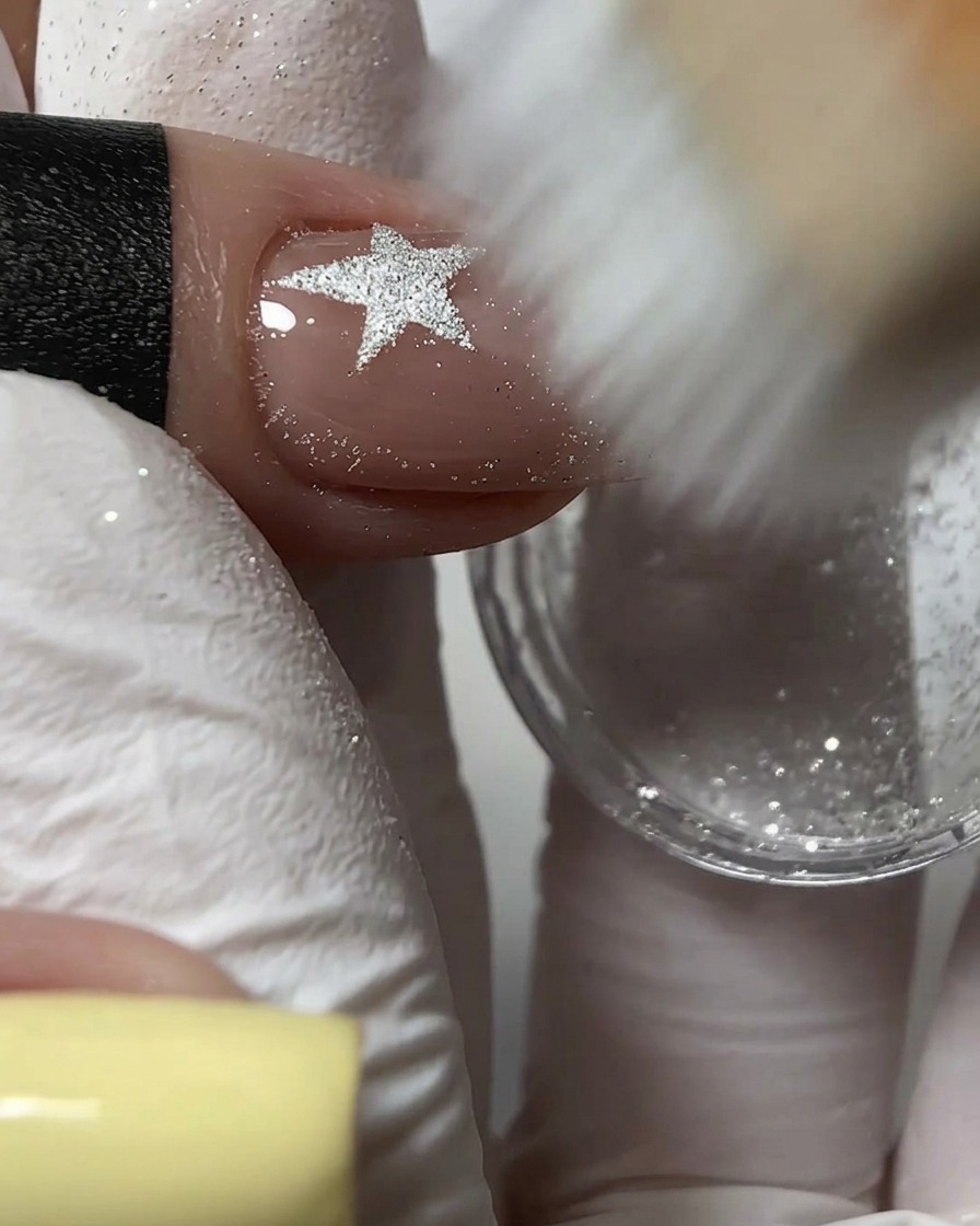 Une brosse à poussière rigide balayant lexcédent de poudre de paillettes argentées sur un ongle texturé.
