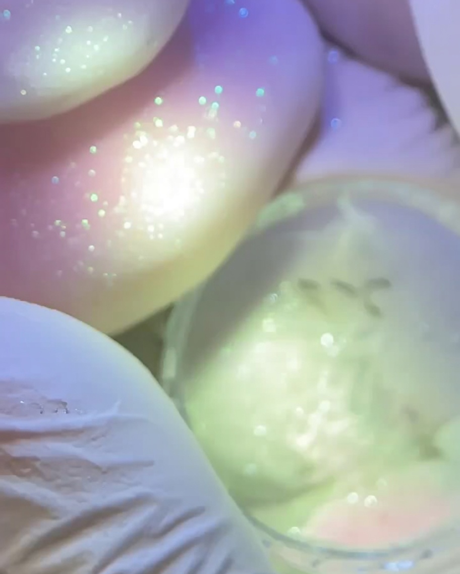 Main gantée tenant une lampe de polymérisation au-dessus dun ongle préparé avec une étoile rose texturée.
