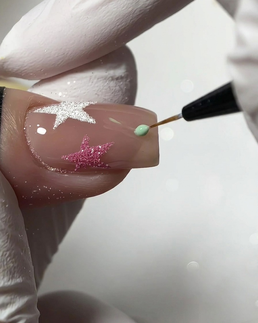 Un pinceau liner fin appliquant une petite goutte de gel vert menthe pour créer une forme détoile sur un ongle nude.